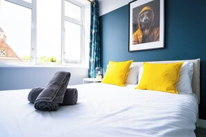 Ein Hotelzimmer mit einem Bett, zwei Kissen, einem Handtuch, einem Fenster und einem gerahmten Bild an der Wand.