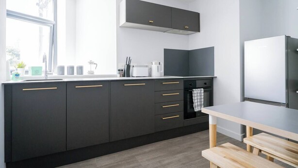 Een moderne keuken met donkere kastjes, een ingebouwde oven en een raam dat voor natuurlijk licht zorgt.