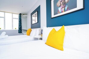 A hotel room with two beds, white bedding, yellow pillows, a framed picture on the wall, and a window with curtains. - #157 Westbourne Beach Retreat - Sleeps 10 (Bournemouth)