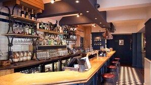Een bar met flessen, glazen en een toonbank met krukken.
