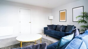 Een moderne woonkamer met een donkerblauwe bank, een witte salontafel en een vloerlamp.