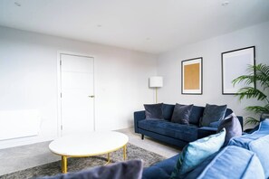 Ein modernes Wohnzimmer mit einem dunkelblauen Sofa, einem weißen Couchtisch und einer Stehlampe.