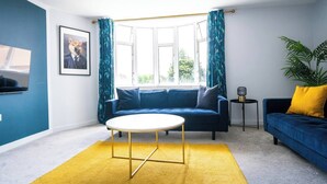 Een moderne woonkamer met een blauwe bank, een ronde salontafel en een geel vloerkleed.