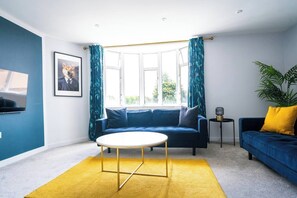 Ein modernes Wohnzimmer mit einem blauen Sofa, einem runden Couchtisch und einem gelben Teppich.