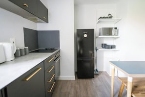 Una cocina compacta con estufa integrada, un refrigerador negro y un microondas sobre un estante blanco.