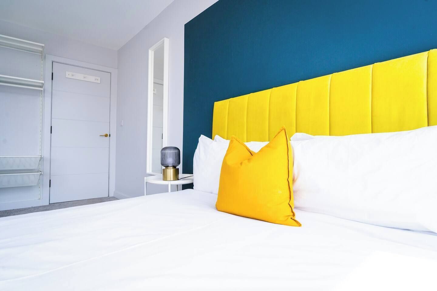 A hotel room with a bed, a bedside table, a lamp, and a door.