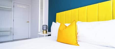 A hotel room with a bed, a bedside table, a lamp, and a door.