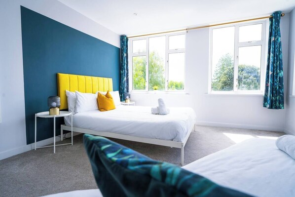 A hotel room with a bed, a bedside table, a lamp, and a window with curtains. - #156 Coastal Stay Bournemouth - Sleeps 10 (Bournemouth)