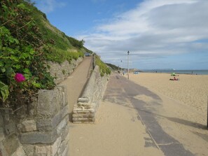 Ein Küstenweg mit einer Steinmauer auf der einen Seite und einem Sandstrand auf der anderen.