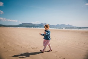 Ein Kind geht über einen sandigen Strand, im Hintergrund Berge.