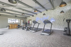 Un gimnasio con cintas de correr, pesas y un letrero de neón en la pared.