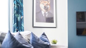 A framed picture of a dog in a suit on a wall, a sofa with pillows, and a small plant on a table. - #150 Bright Apt – Westbourne Area - Sleeps 7 (Bournemouth)