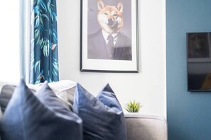 A framed picture of a dog in a suit on a wall, a sofa with pillows, and a small plant on a table. - #150 Bright Apt – Westbourne Area - Sleeps 7 (Bournemouth)