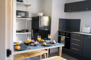 A modern kitchen with a dining table set for breakfast, including croissants, juice, and a bottle of wine. - #150 Bright Apt – Westbourne Area - Sleeps 7 (Bournemouth)
