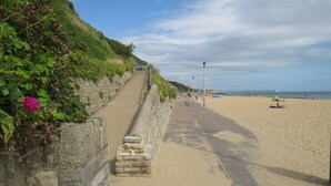 A coastal walkway with a stone wall on one side and a sandy beach on the other. - #150 Bright Apt – Westbourne Area - Sleeps 7 (Bournemouth)