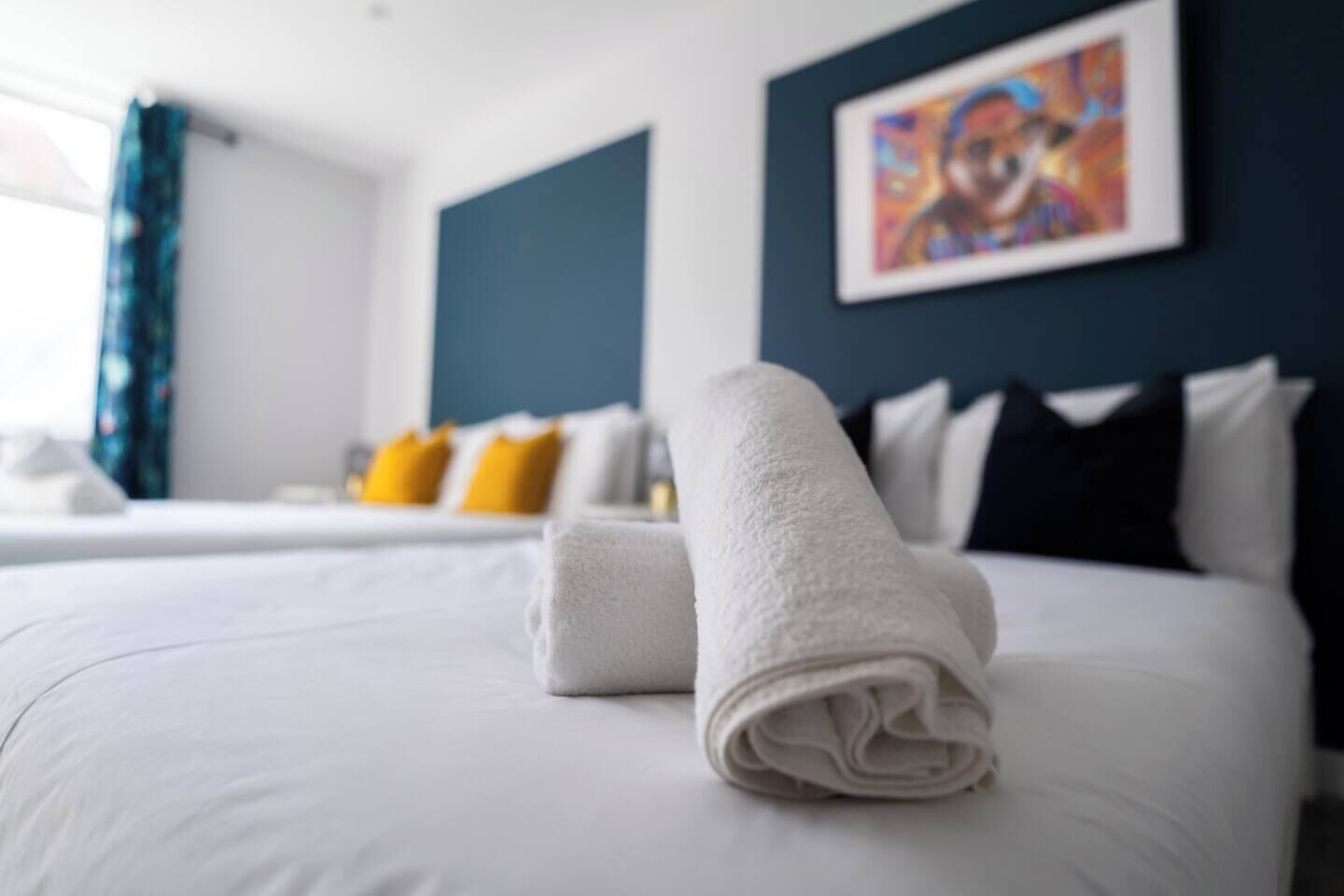 Ein Hotelzimmer mit einem ordentlich bezogenen Bett, einem Bild an der Wand und einem Fenster mit Vorhängen.