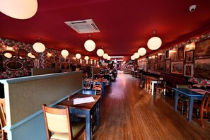 Een restaurantinterieur met houten vloeren, ronde plafondlampen en bloemenbehang.