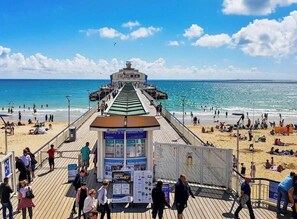 A pier with a ticket booth and information signs, leading to a beach with people and umbrellas. - #150 Bright Apt – Westbourne Area - Sleeps 7 (Bournemouth)