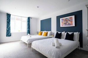 A hotel room with two beds, a large window with curtains, a painting on the wall, and a small table with a lamp. - #150 Bright Apt – Westbourne Area - Sleeps 7 (Bournemouth)