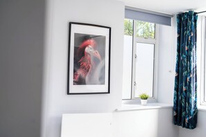 Een kamer met een lijstwerk kunstwerk aan de muur, een raam met uitzicht en een bloempot op de vensterbank.
