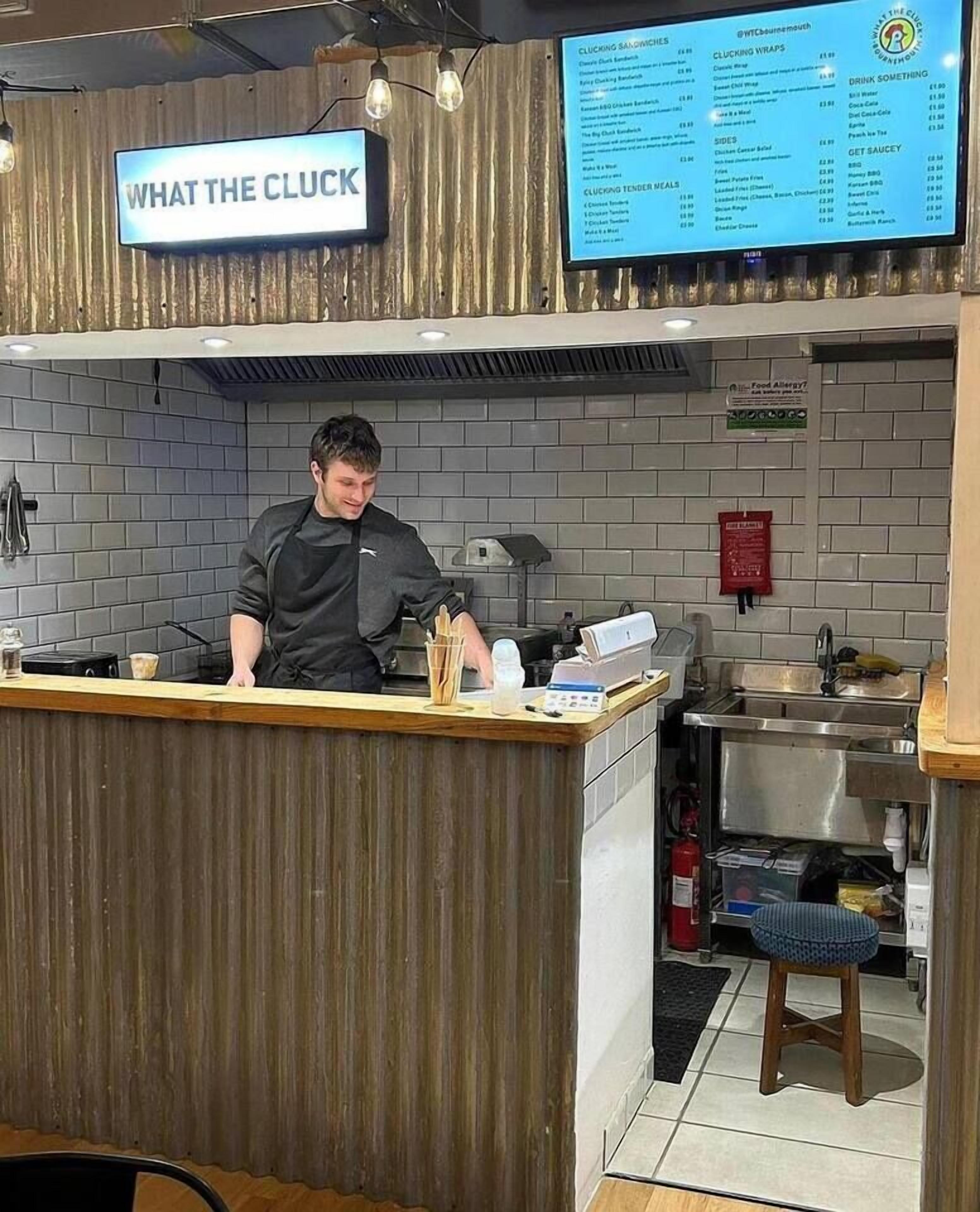 A restaurant counter with a menu board above, a kitchen area with a fire extinguisher, and a sign indicating food allergies.