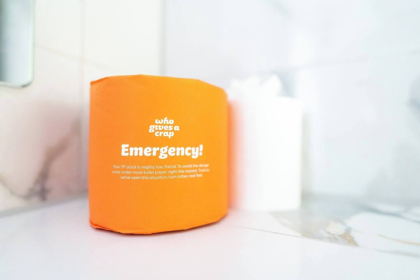 Eine Rolle Toilettenpapier mit einem orangefarbenen Etikett, auf dem 'who gives a crap Emergency!' steht.