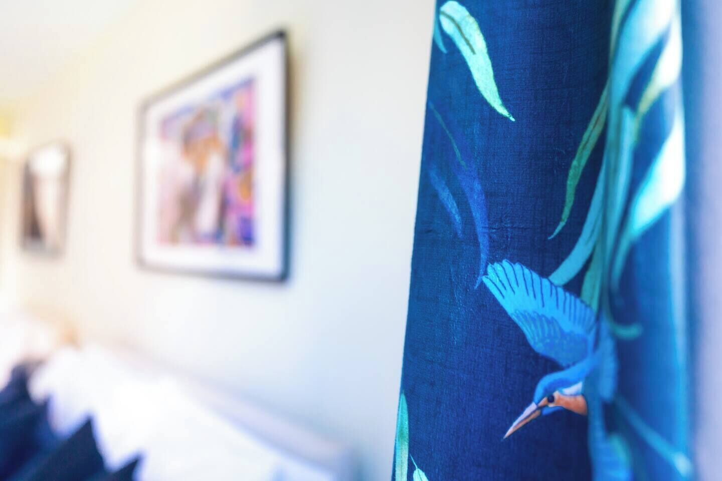 Ein Hotelzimmer mit einem Bett, einem Wandbild und einem Vorhang mit Vogelmotiv.