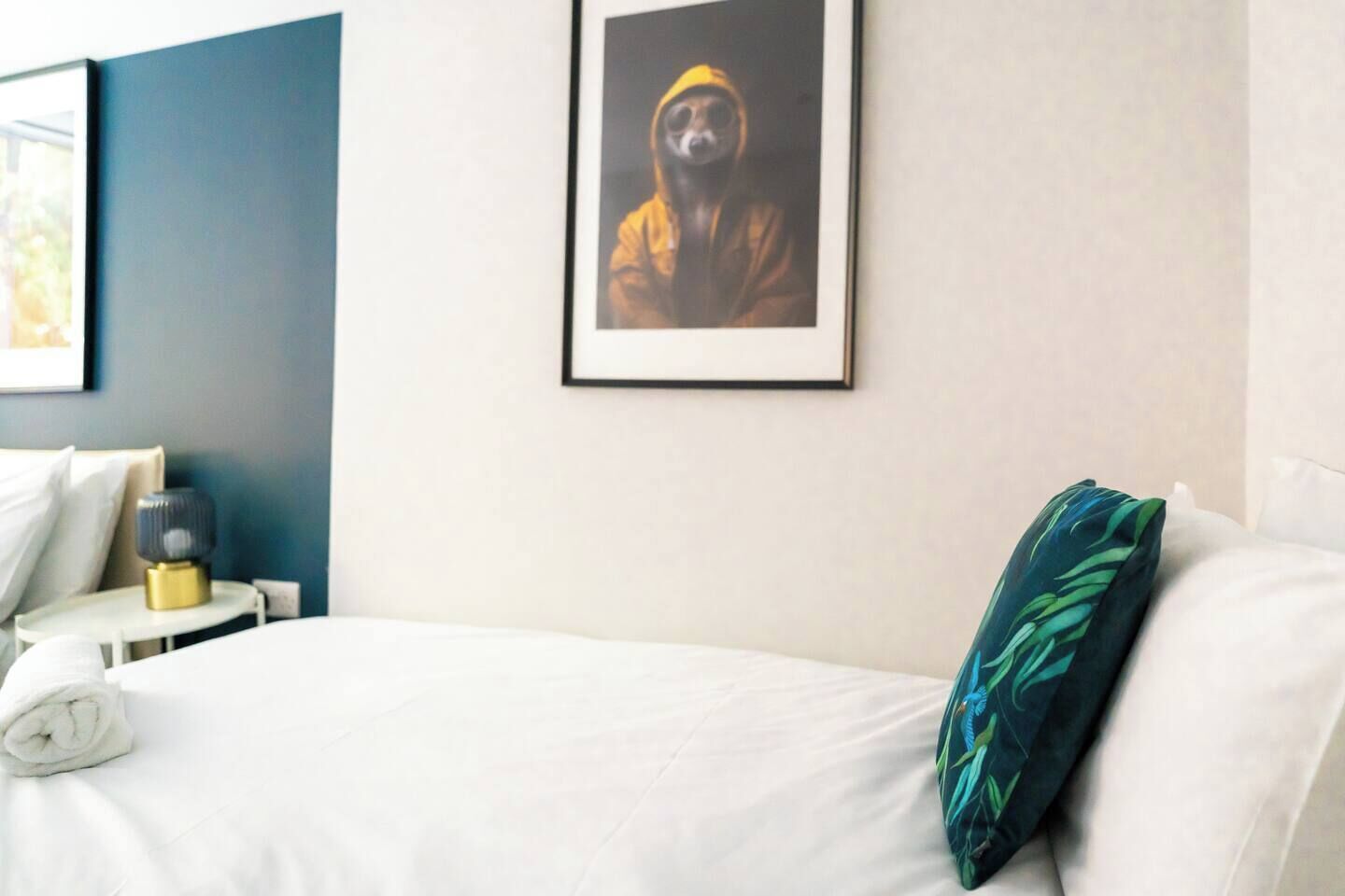Ein Hotelzimmer mit Bett, Kissen, Nachttisch und einem gerahmten Bild an der Wand.