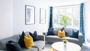 Ein modernes Wohnzimmer mit zwei grauen Sofas, gelb-schwarzen Kissen, einem runden Couchtisch und einem großen Fenster mit Vorhängen.