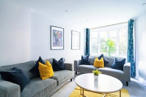 Ein modernes Wohnzimmer mit zwei grauen Sofas, gelb-schwarzen Kissen, einem weißen Couchtisch und gerahmten Kunstwerken an der Wand.