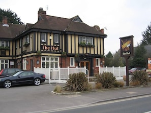 Ein traditionelles Pub namens 'The Hut' mit weißem Zaun und Blumentöpfen davor.
