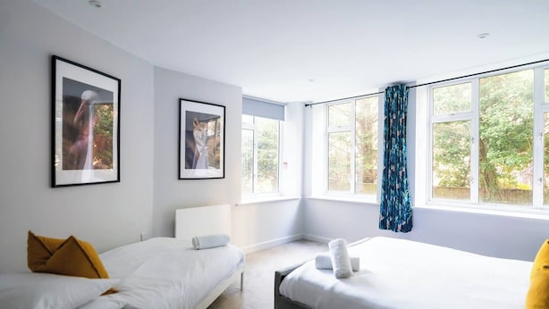 Ein modernes Schlafzimmer mit zwei Betten, großen Fenstern und gerahmten Bildern an der Wand.