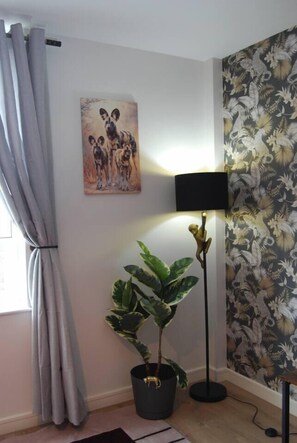 Una habitación con una planta en maceta, una lámpara de pie, un cuadro y una cortina.