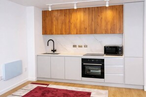 A modern kitchen with white cabinets, a black oven, a microwave, and a red rug. - #146 Urban Stay at Sapphire Court - Sleeps 6 (West Midlands)