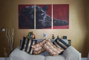 Habitación con sofá, tres cuadros en la pared de un guepardo negro, una pequeña estatua y un cartel que prohíbe fumar.