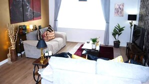 A living room with a sofa, a coffee table, a TV, and a painting on the wall. - #146 Urban Stay at Sapphire Court - Sleeps 6 (West Midlands)