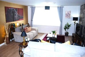 A living room with a sofa, a coffee table, a TV, and a painting on the wall. - #146 Urban Stay at Sapphire Court - Sleeps 6 (West Midlands)