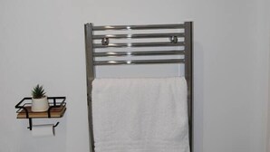 A bathroom with a towel rack, a framed picture of a giraffe and lion, and a small shelf with a plant. - #146 Urban Stay at Sapphire Court - Sleeps 6 (West Midlands)