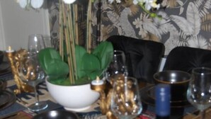 A dining table set with plates, glasses, a bottle, and a vase with flowers. - #146 Urban Stay at Sapphire Court - Sleeps 6 (West Midlands)