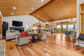 A spacious living area with a wooden ceiling, a fireplace, a television, and a view of the outdoors. - The Residence at Freshwater Bay (Port Angeles)