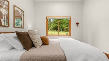 Een slaapkamer met een groot bed, een raam met uitzicht op groen en kunstwerken in een lijst aan de muur.