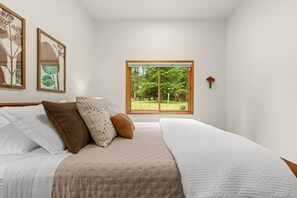 Ein Schlafzimmer mit einem großen Bett, einem Fenster mit Blick auf Grünflächen und gerahmten Kunstwerken an der Wand.