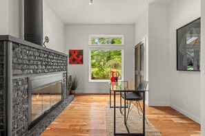 A modern interior with a fireplace, a dining area with a glass table, and a view of greenery outside. - The Residence at Freshwater Bay (Port Angeles)