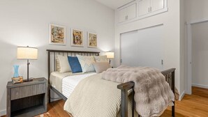 A bedroom with a bed, bedside tables, wall art, a wardrobe, and a door. - The Residence at Freshwater Bay (Port Angeles)