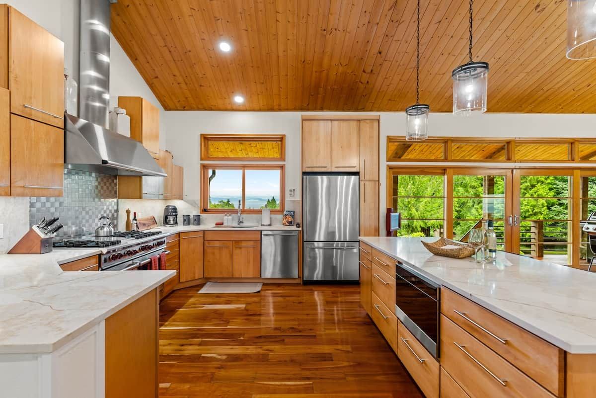 Une cuisine moderne avec des meubles en bois, des appareils électroménagers en acier inoxydable et une vue sur la verdure environnante.