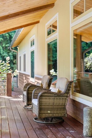A covered porch with wicker chairs and a wooden deck. - The Residence at Freshwater Bay (Port Angeles)