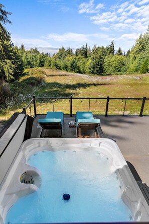 Uma banheira de hidromassagem com duas espreguiçadeiras, cercada por um deck com vista para uma paisagem arborizada.
