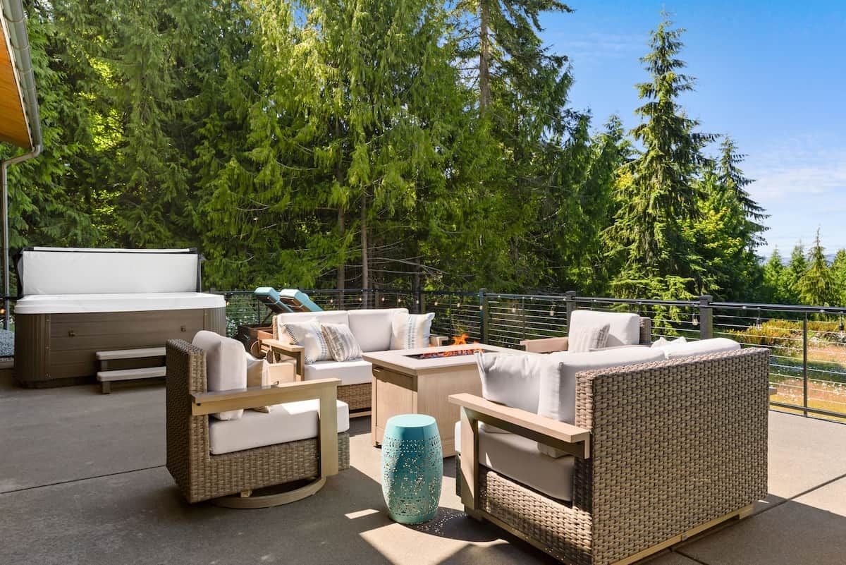 Een terras buiten met rieten meubilair, een hottub en uitzicht op een bos.