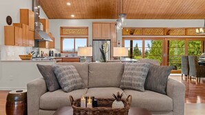 A modern living room with a sectional sofa, a dining area, and a kitchen with wooden cabinets. - The Residence at Freshwater Bay (Port Angeles)