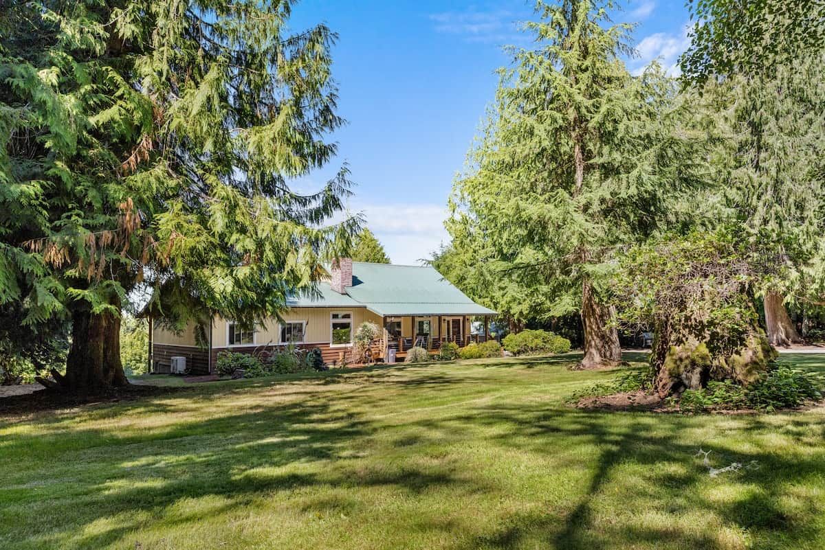 Uma casa com telhado verde, rodeada por árvores grandes e um gramado bem cuidado.